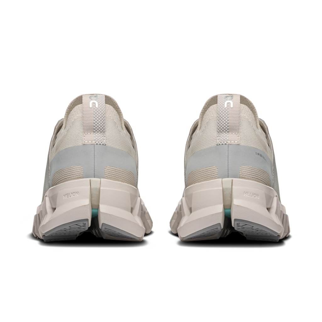 A pair of minimalist running shoes shown from the rear, featuring a chunky midsole, light gray and beige mesh upper, and a small teal accent near the outsole.