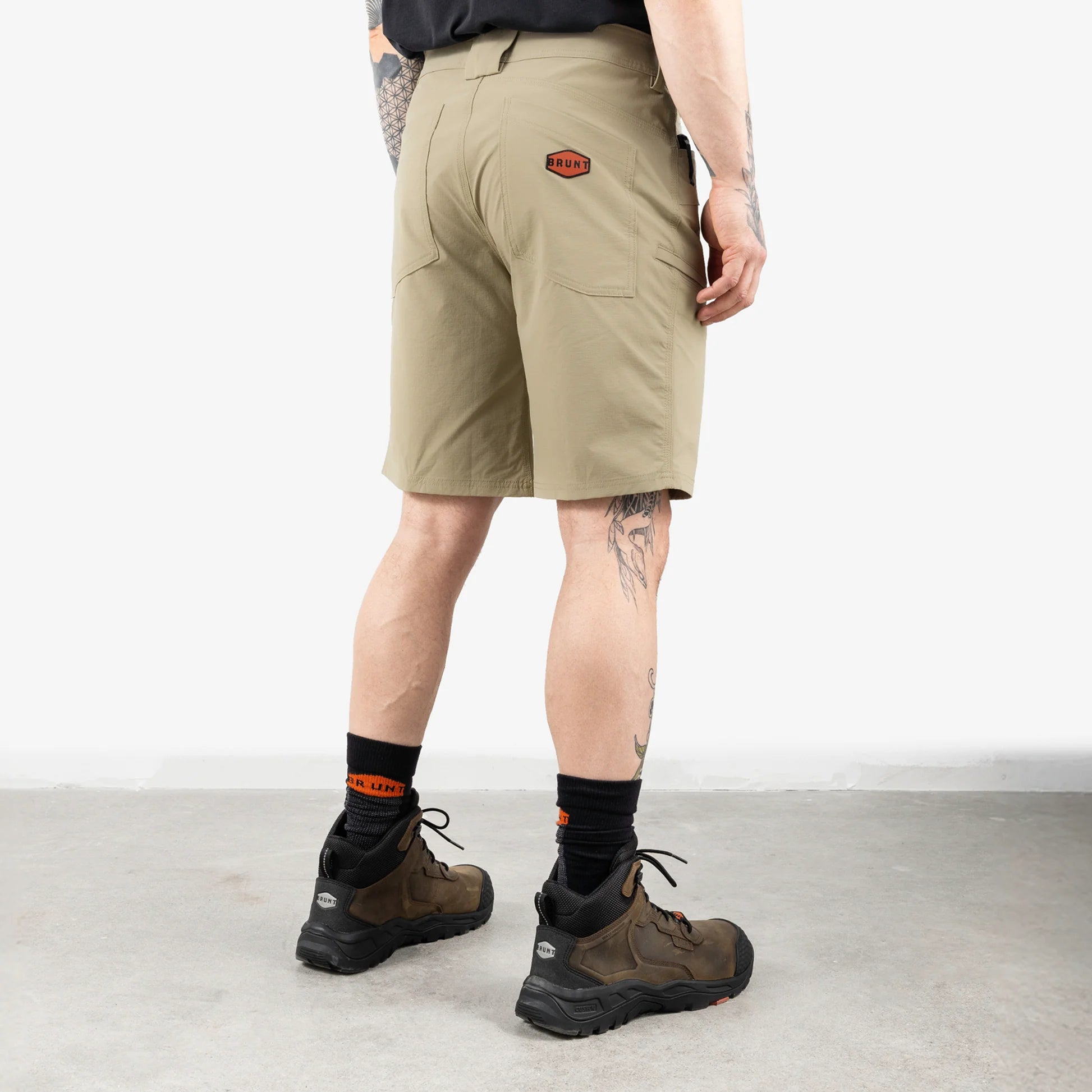 Person wearing beige shorts with a brand logo, black socks, and hiking boots on a white background