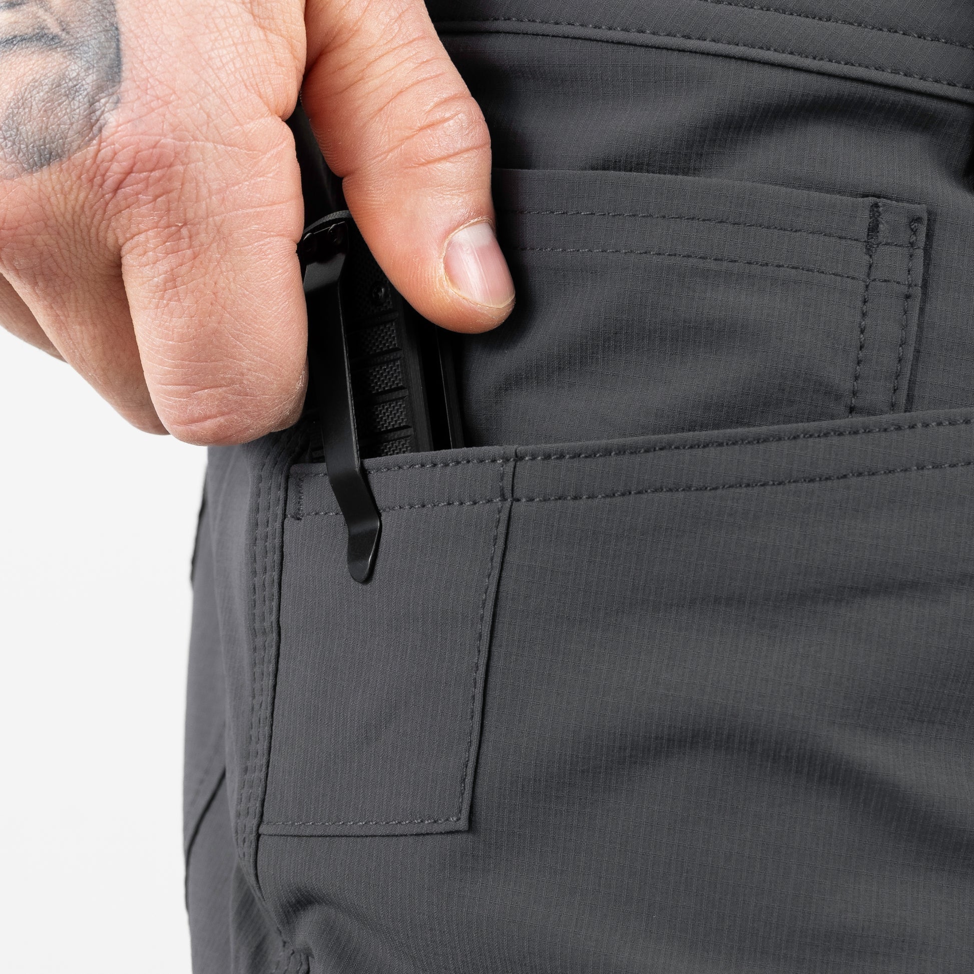 Person opening a pocket on dark gray pants with a white background