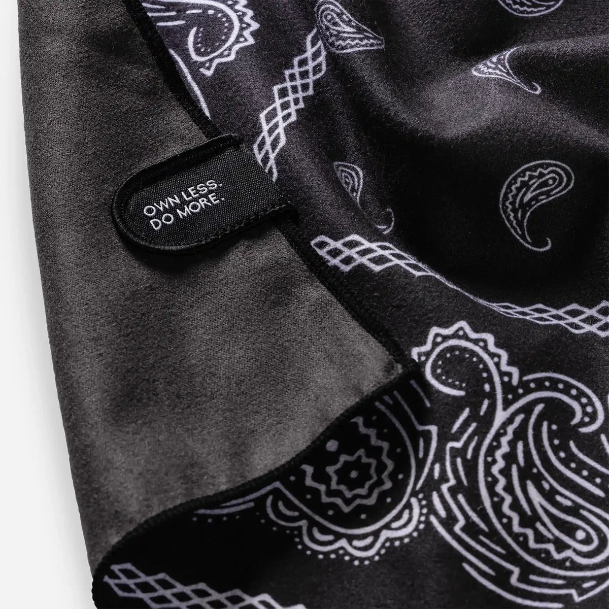Black bandana with white paisley patterns and a visible brand tag on a light gray background