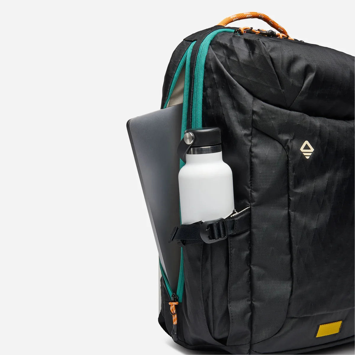 A black backpack with teal zipper accents and an orange top handle, shown on a light gray background with a laptop and white bottle in its side pockets.