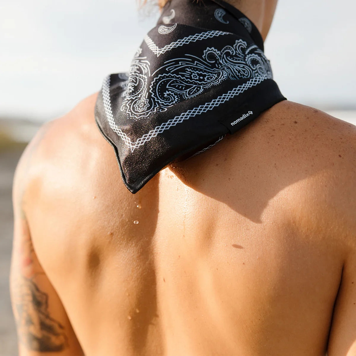 Person wearing a black bandana with white patterns on their shoulder outdoors.
