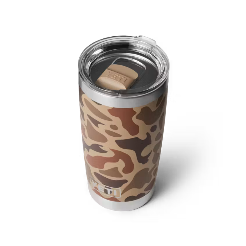 A YETI insulated travel tumbler with a brown and beige camouflage pattern, featuring a clear lid and a tan YETI logo on the lid.