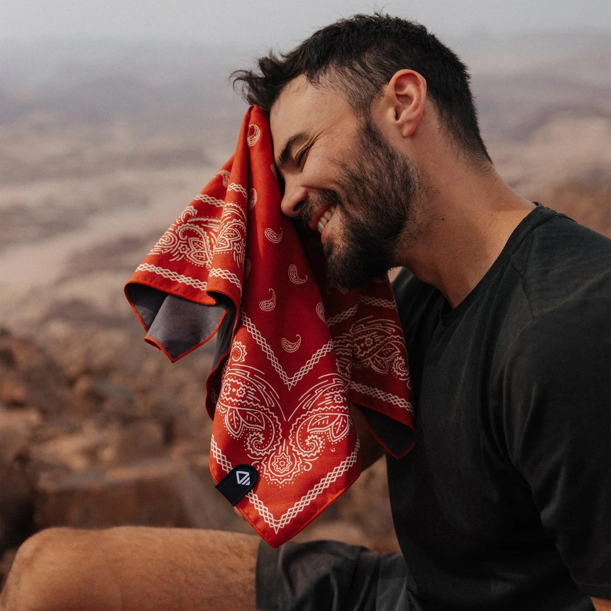 Man with a red bandana wiping his face against a mountainous background