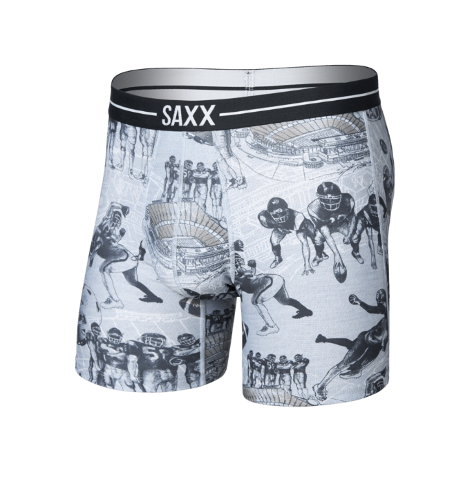 A pair of SAXX boxer briefs featuring a black and white football player collage print on a light gray base, with a black elastic waistband displaying the white SAXX logo.