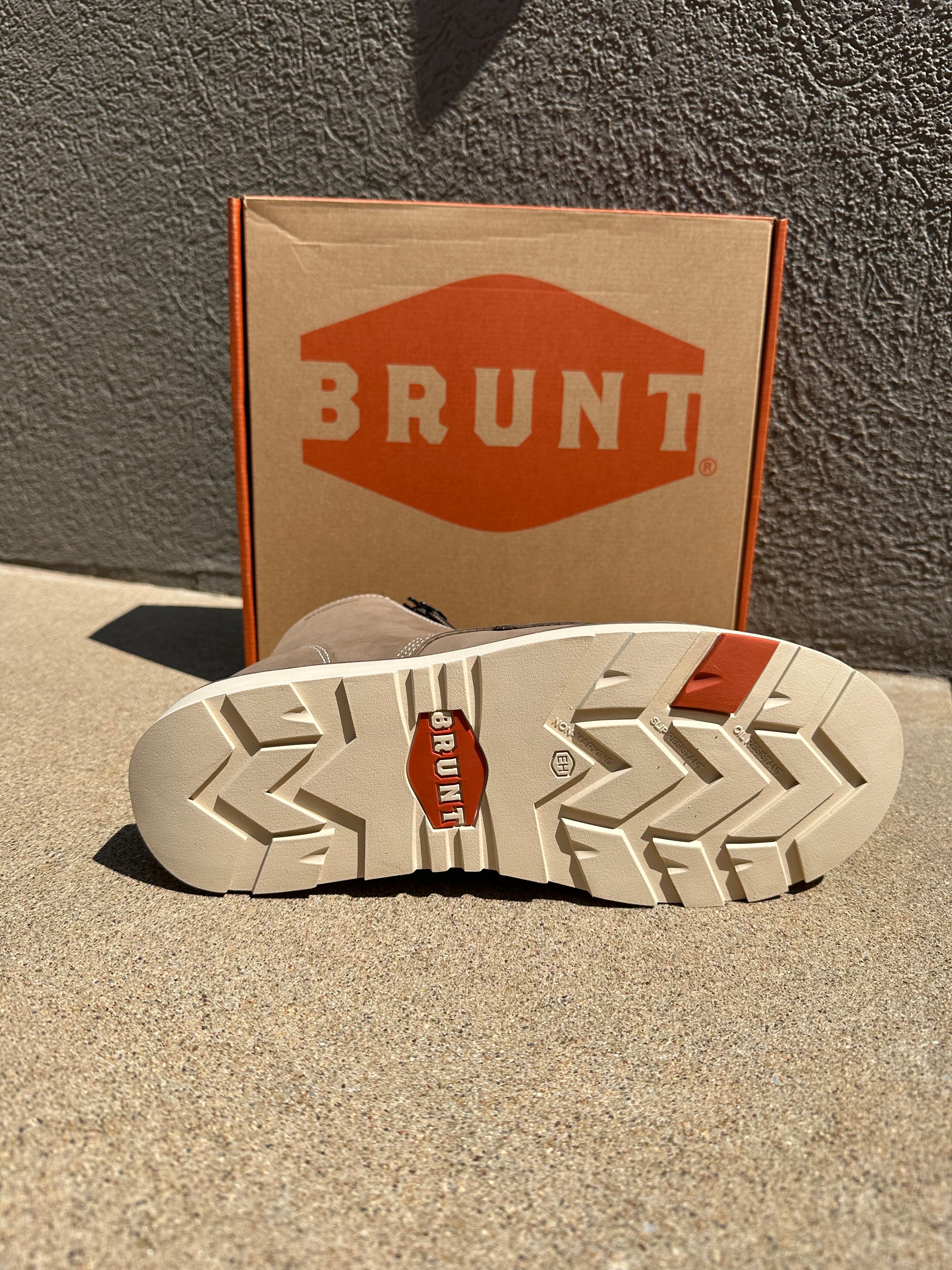 A close-up of a Brunt boot sole showing its textured tread pattern and orange logo, with the branded cardboard box standing behind it against a gray textured wall.