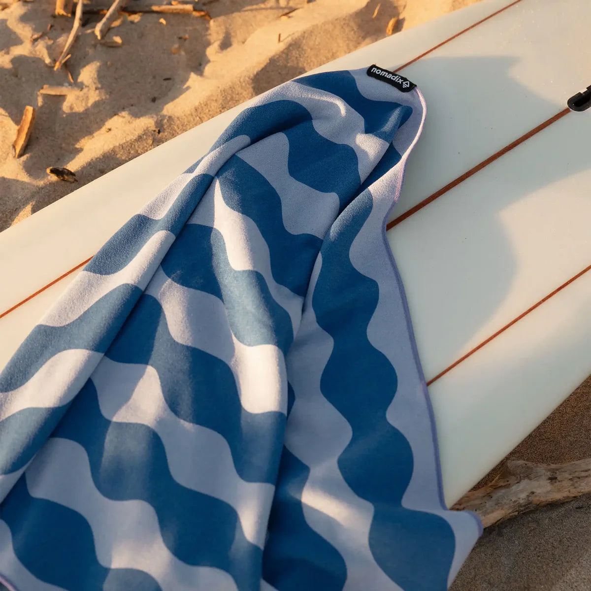 Blue and white patterned towel draped over a surfboard on sandy beach