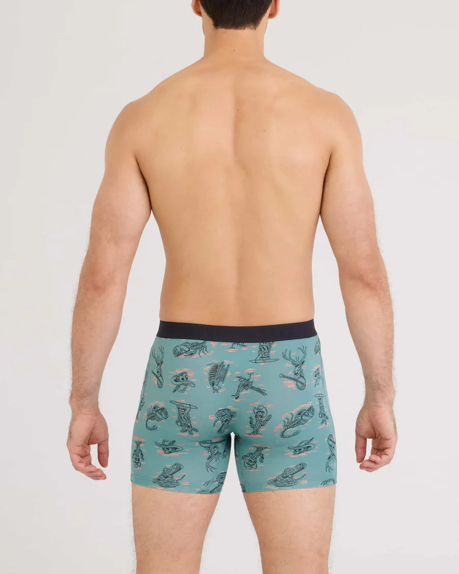 Man wearing teal boxer briefs with a pattern on a plain background