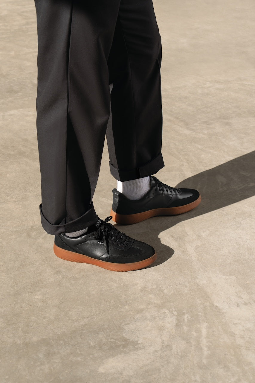 Person wearing black shoes with brown soles on a concrete surface