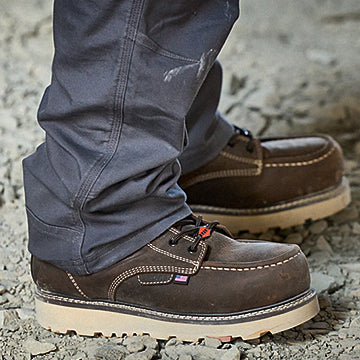 Brown work boots worn with gray pants on a rocky ground